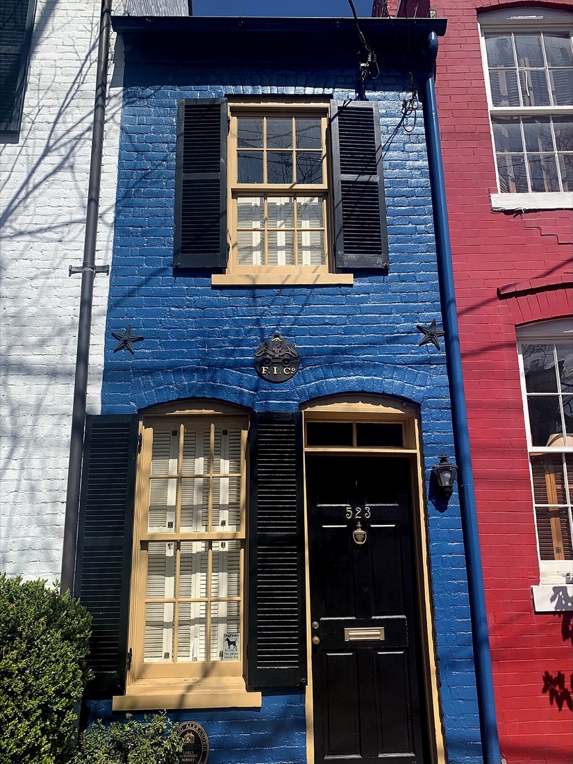 Facciata blu stretta di una casa tra due edifici, con una finestra e una porta