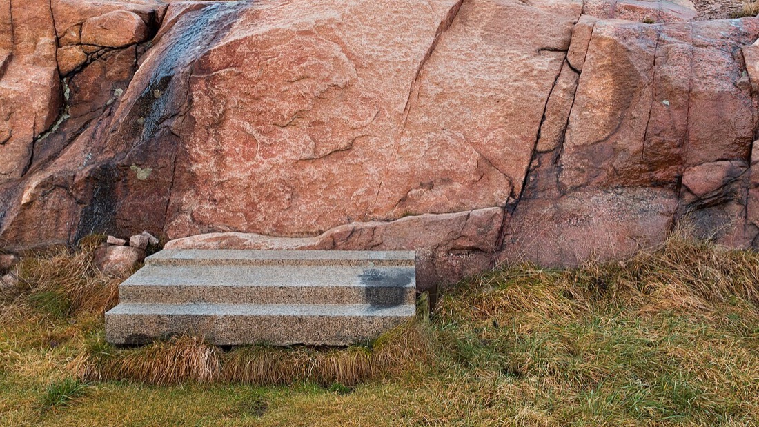 Tre gradini di granito appoggiati sull'erba davanti a una parete di roccia
